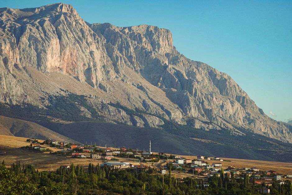 A breathtaking landscape of a small town nestled at the base of grand rocky mountains under a clear blue sky.