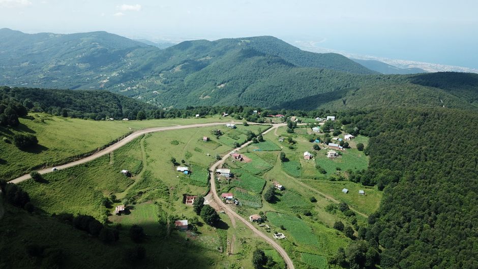 Aerial perspective of a scenic rural village nestled in lush green mountains under clear skies.
