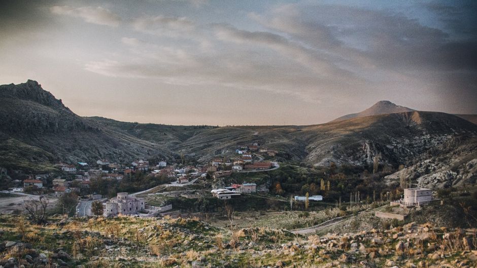 Peaceful rural village nestled in a serene valley with mountain backdrop at dusk.
